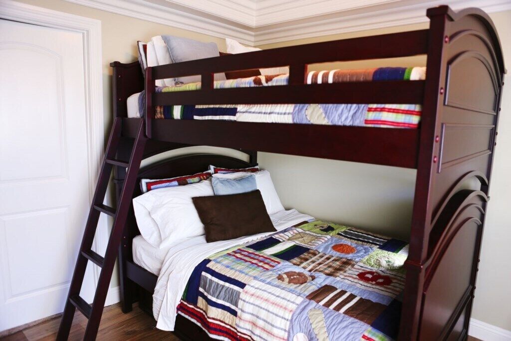 A bunk bed with a ladder, a quilt, and a door.