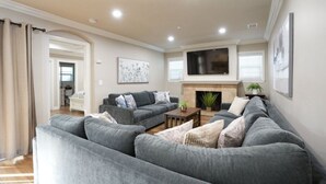 Ein Wohnzimmer mit grauen Sofas, einem flachbildfernseher über einem Kamin und einem Gemälde an der Wand.