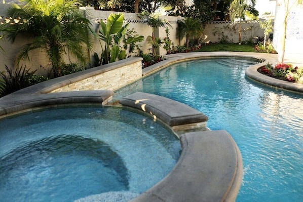 A swimming pool with a curved edge, surrounded by a brick wall and lush greenery.