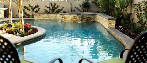 A swimming pool with a stone edge, surrounded by lush greenery and a brick wall.