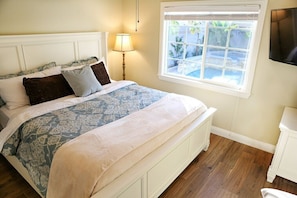 A bedroom with a bed, a bedside lamp, a window, and a TV on the wall.