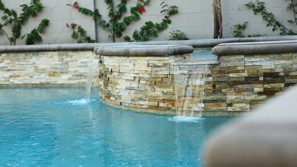 Ein Schwimmbecken mit einer Steinmauer und einem Wasserfall.