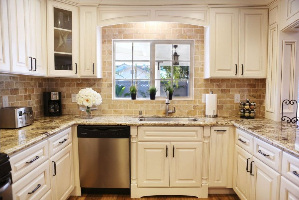 A kitchen with white cabinets, a dishwasher, a granite countertop, and a window with plants.