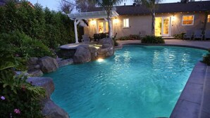 Ein Schwimmbecken mit Felsen und eine Terrassenanlage mit Gartenmöbeln.