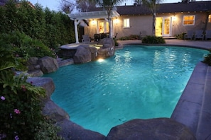 Une piscine agrémentée d’un élément rocheux et un espace patio avec des meubles d’extérieur.