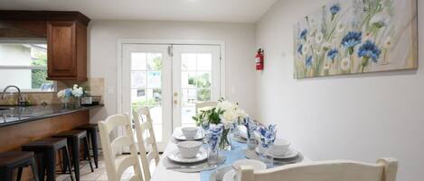 A dining area with a table set for four, chairs, a kitchen area with a counter, and a door leading outside.