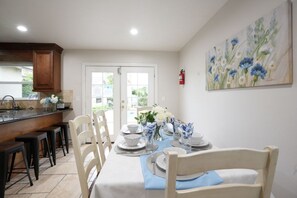 A dining area with a table set for four, chairs, a kitchen area with a counter, and a door leading outside. - Incredible 5 Bedroom, 4 Bath, Rock Pool & Jacuzzi Home, 1/2 Mile Walk To Disney (Anaheim)