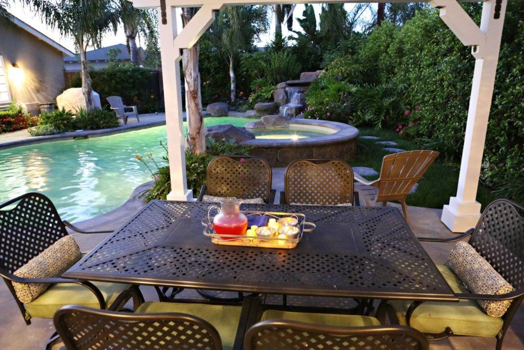 An outdoor patio with a pool, chairs, and a table with a drink tray.