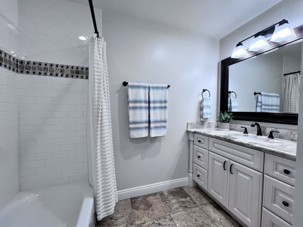 Un baño con ducha, un lavabo con espejo y un perchero para toallas.