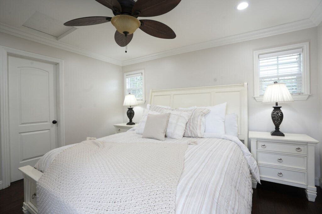 A bedroom with a bed, nightstands, a ceiling fan, and a window with blinds.