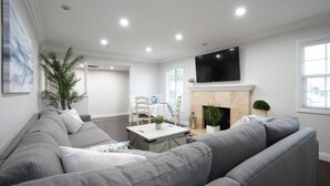 Ein Wohnzimmer mit grauem Sofa, einem Flachbildfernseher, einem Kamin und einem Essbereich mit Tisch und Stühlen.
