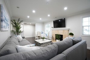 A living room with a gray sofa, a flat-screen TV, a fireplace, and a dining area with a table and chairs. - Incredible 5 Bedroom, 4 Bath, Rock Pool & Jacuzzi Home, 1/2 Mile Walk To Disney (Anaheim)