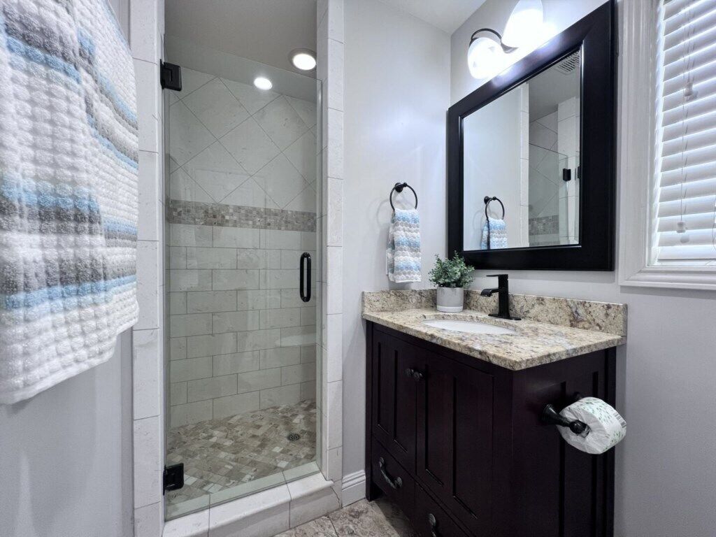 A bathroom with a glass-enclosed shower, a sink with a dark cabinet, a mirror, and a towel rack.