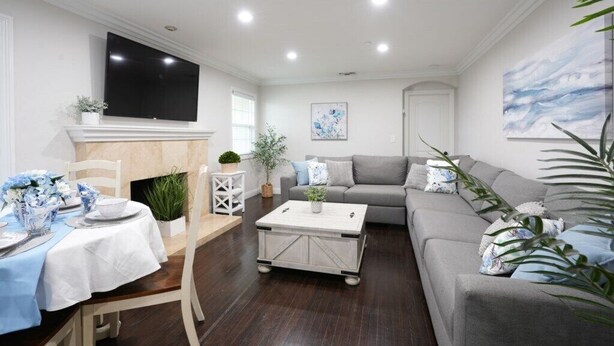 Ein Wohnzimmer mit einer Couch, einem Couchtisch, einem an der Wand befestigten Fernseher und einer Essecke mit Tisch für zwei Personen.