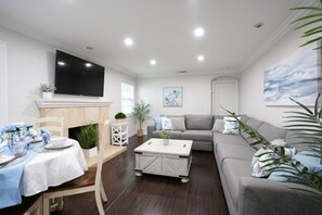 A living room with a sofa, a coffee table, a TV mounted on the wall, and a dining area with a table set for two. - Incredible 5 Bedroom, 4 Bath, Rock Pool & Jacuzzi Home, 1/2 Mile Walk To Disney (Anaheim)