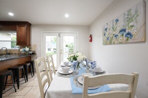 A dining area with a table set for four, chairs, a kitchen area with a counter, and a door leading outside. - Incredible 5 Bedroom, 4 Bath, Rock Pool & Jacuzzi Home, 1/2 Mile Walk To Disney (Anaheim)