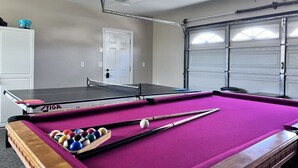 Ein Billardtisch mit rosa Filzoberfläche, ein Tischtennistisch und eine Tür im Hintergrund.