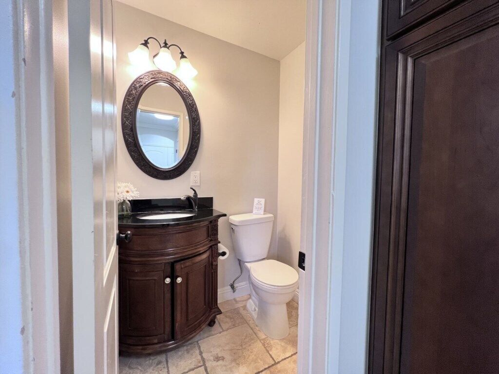 A bathroom with a dark wooden vanity, a white toilet, and a mirror with lights.