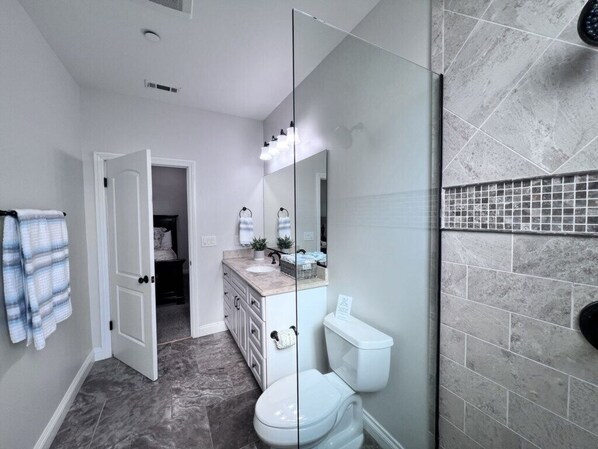 A bathroom with a glass shower enclosure, a toilet, and a vanity with a mirror.
