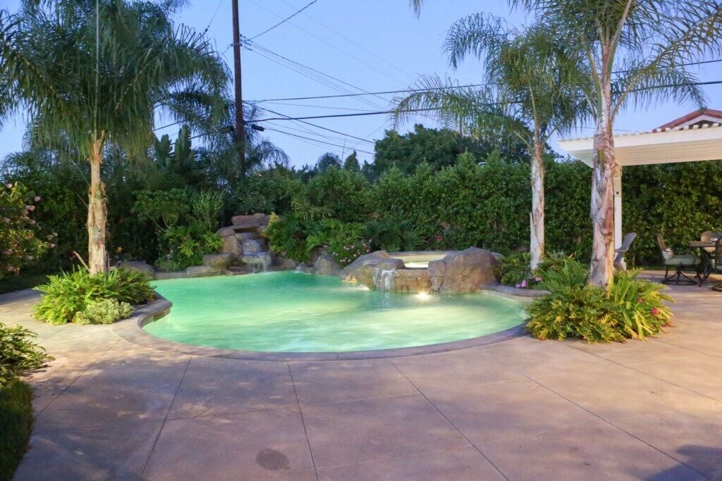 A swimming pool with a natural rock feature, surrounded by tropical plants and trees.