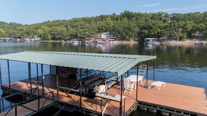 Un muelle con una zona de estar techada, un bote y vistas a casas al otro lado del agua.