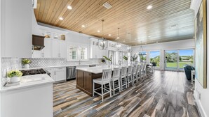 Una cocina moderna con armarios blancos, techo de madera y una isla grande con taburetes de bar.