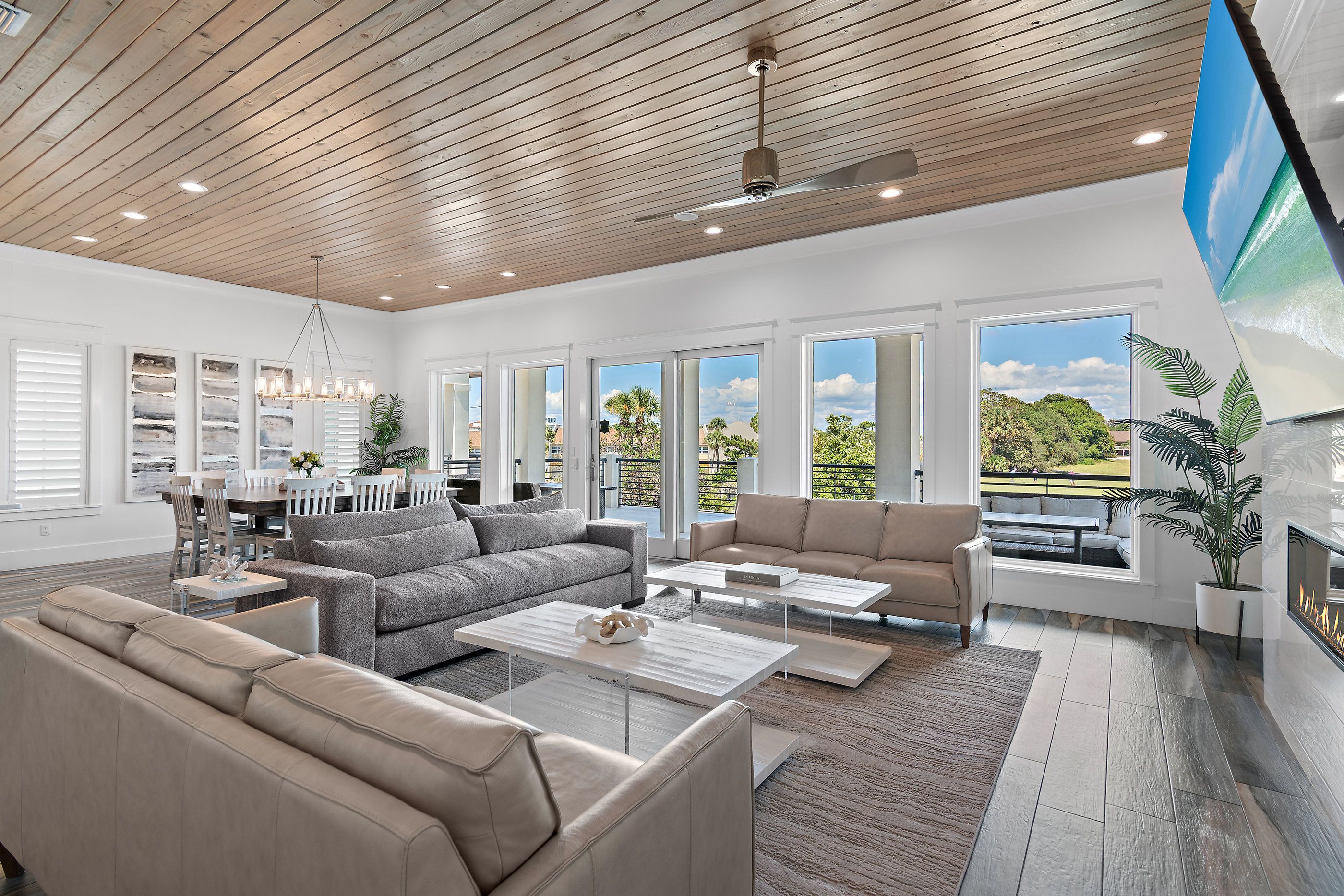 A spacious living room with a high ceiling, large windows, and a fireplace.