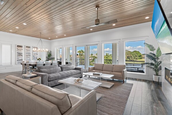 A spacious living room with a high ceiling, large windows, and a fireplace.