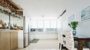 Een moderne keuken met witte kastjes, een roestvrijstalen koelkast, een magnetron, en een eethoek met een houten tafel en stoelen.