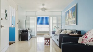 Een moderne woonkamer met een bank, een salontafel en een televisie. Er is een deur naar een balkon met blauwe gordijnen.