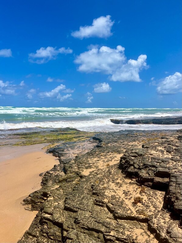 A rocky beach with waves crashing onto the shore under a clear blue sky. - Seaside Apt Steps to Breathtaking Sunrise and Beautiful Playa Azul in Luquillo (Luquillo)