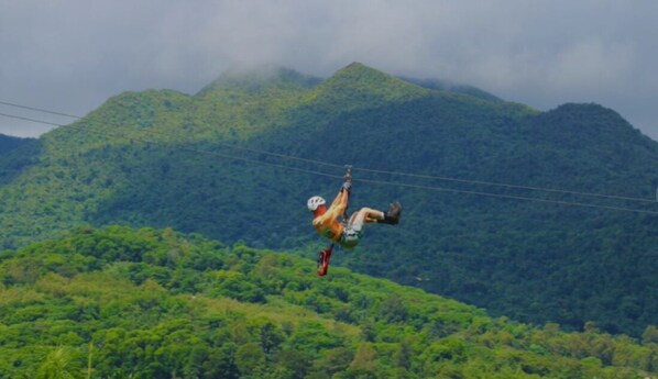 A person in a harness suspended over a mountainous landscape with dense greenery. - Seaside Apt Steps to Breathtaking Sunrise and Beautiful Playa Azul in Luquillo (Luquillo)