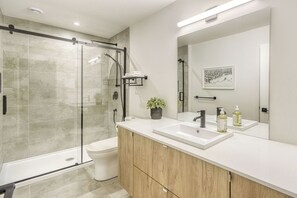Enjoy a refreshing shower in the bathroom, featuring a glass-enclosed shower, white toilet, and vanity with a large mirror.