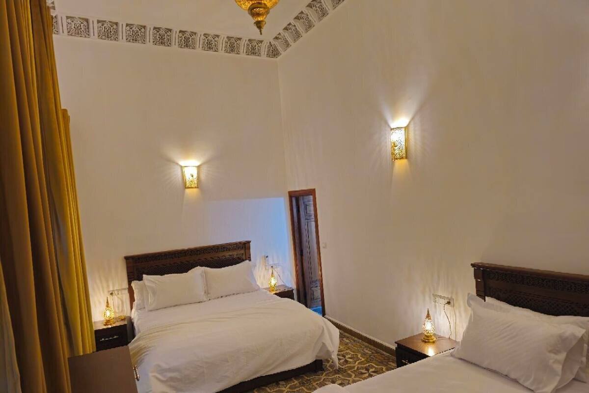 A hotel room with two beds, a patterned floor, and wall-mounted lights.