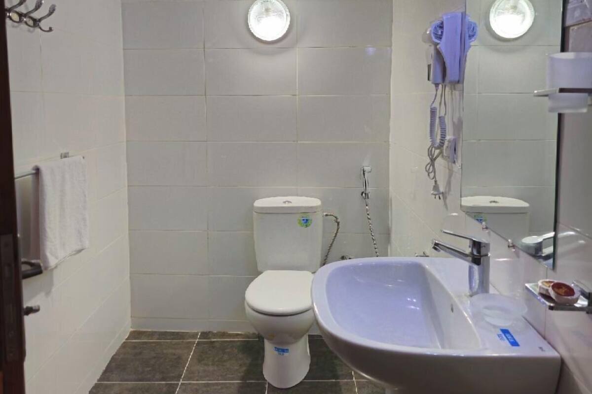 A bathroom with a toilet, sink, and mirror. There are two round lights on the ceiling, and a towel rack on the wall.