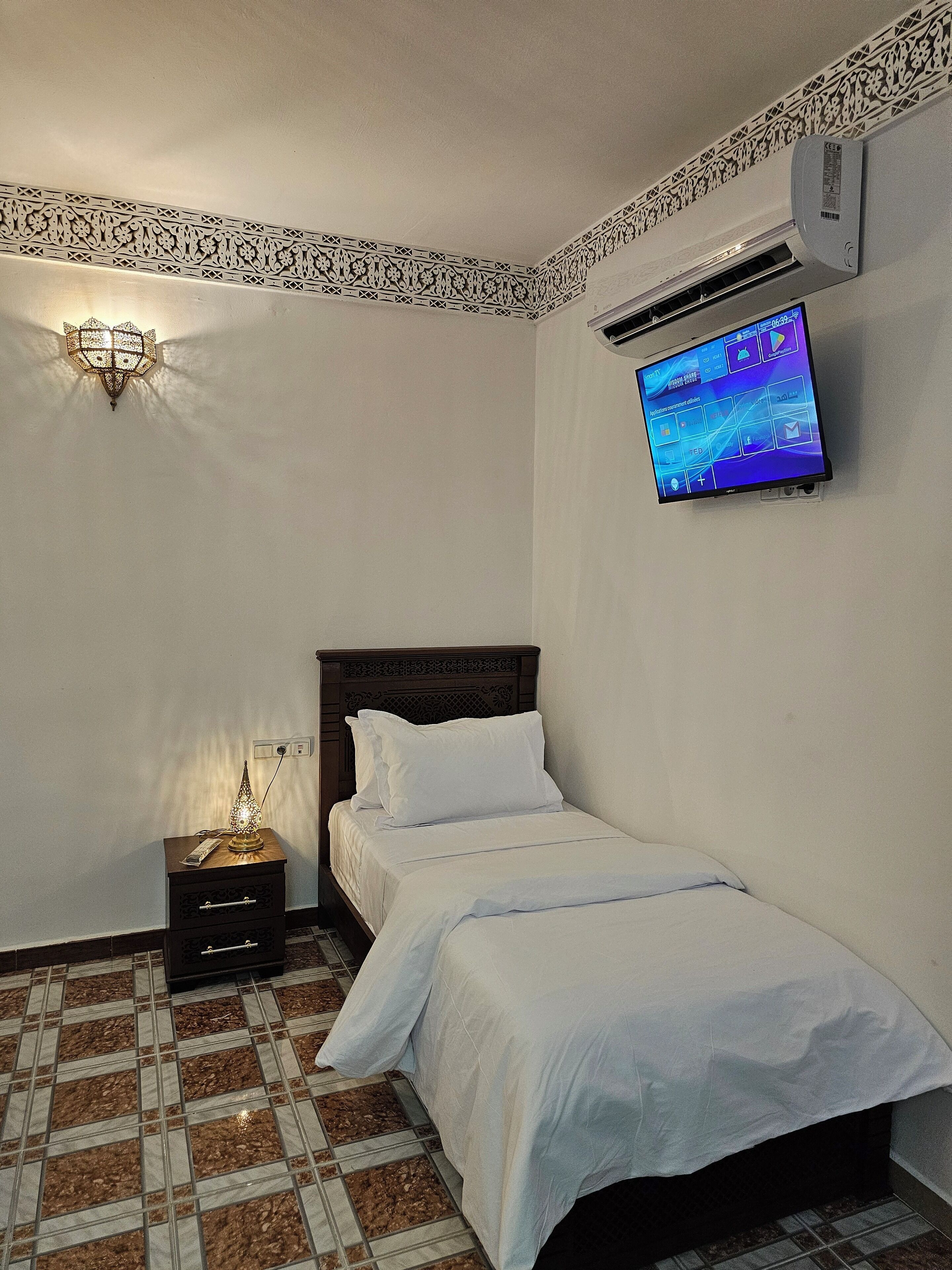 A bedroom with a bed, a nightstand, a wall-mounted TV, and an air conditioning unit.