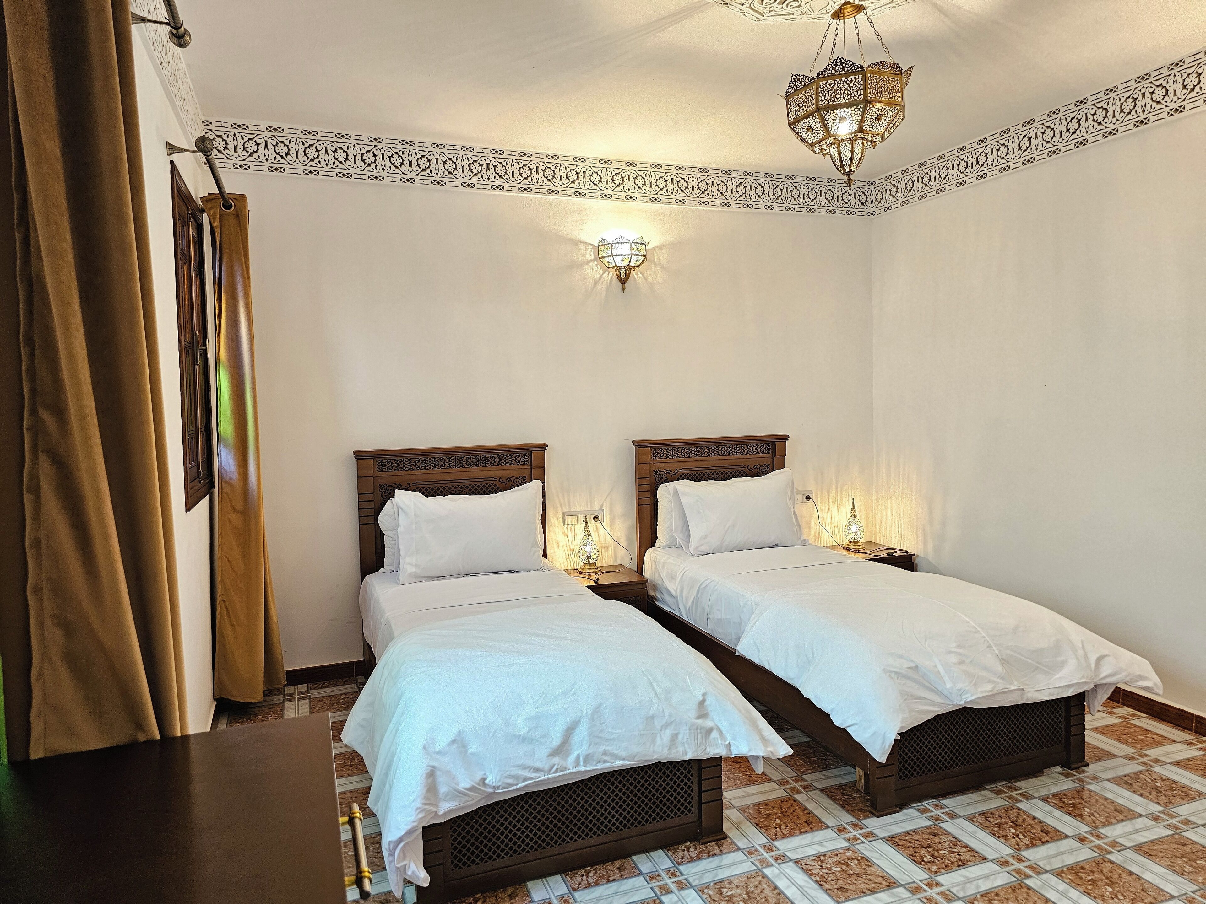 A room with two beds, a chandelier, patterned wall decor, and a curtain.