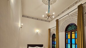 Ένα δωμάτιο ξενοδοχείου με δύο κρεβάτια, διακοσμητικά φωτιστικά τοίχου, ένα πολυέλαιο και ένα παράθυρο με βιτρό.