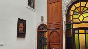Ένας παραδοσιακός μαροκινός εσωτερικός χώρος με μια ξύλινη πόρτα, περίτεχνες διακοσμήσεις στους τοίχους, έναν κόκκινο καναπέ και ένα τραπέζι φαγητού με καρέκλες.