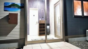 A sliding glass door leading to a room with a wooden floor, a white door, and a small shelf with a basket. - Racine Yakushima (Yakushima)