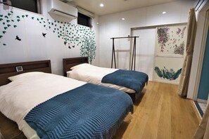 A hotel room with two beds, a window with a view, a wall with leaf patterns, and a door with a plant mural. - Racine Yakushima (Yakushima)