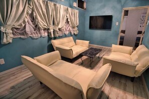A room with a blue wall, a wooden floor, and beige furniture including two armchairs and a sofa. There is a small table in the center. - Racine Yakushima (Yakushima)
