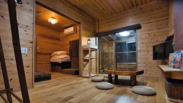 A wooden interior with a bench, pillows, and a television. - Racine Yakushima (Yakushima)