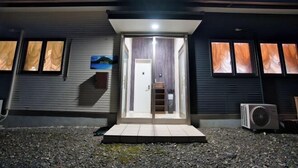 A modern building with a glass entrance, a small outdoor seating area, and an air conditioning unit. - Racine Yakushima (Yakushima)