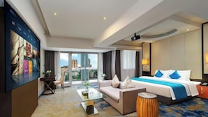 A hotel room with a large bed, a sofa, a coffee table, a TV mounted on the wall, and a view of the city through large windows. - LiSheng Yijia Hotel (Chengdu)