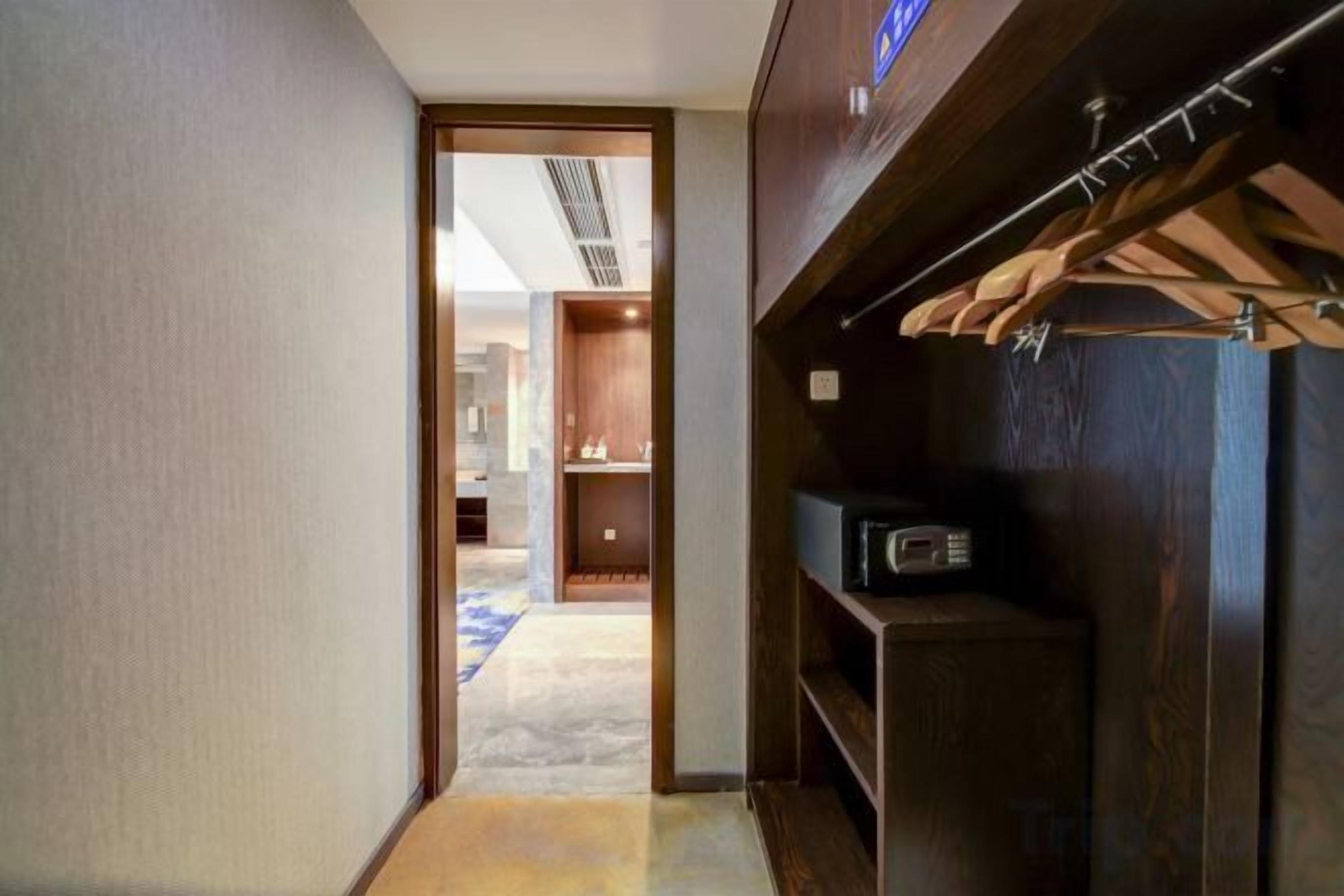 A hallway leading to a room with a wooden wardrobe and a television.