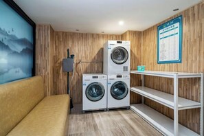 Un lavadero con dos lavadoras apiladas, una pared de madera, un sofá y un tablón de anuncios.