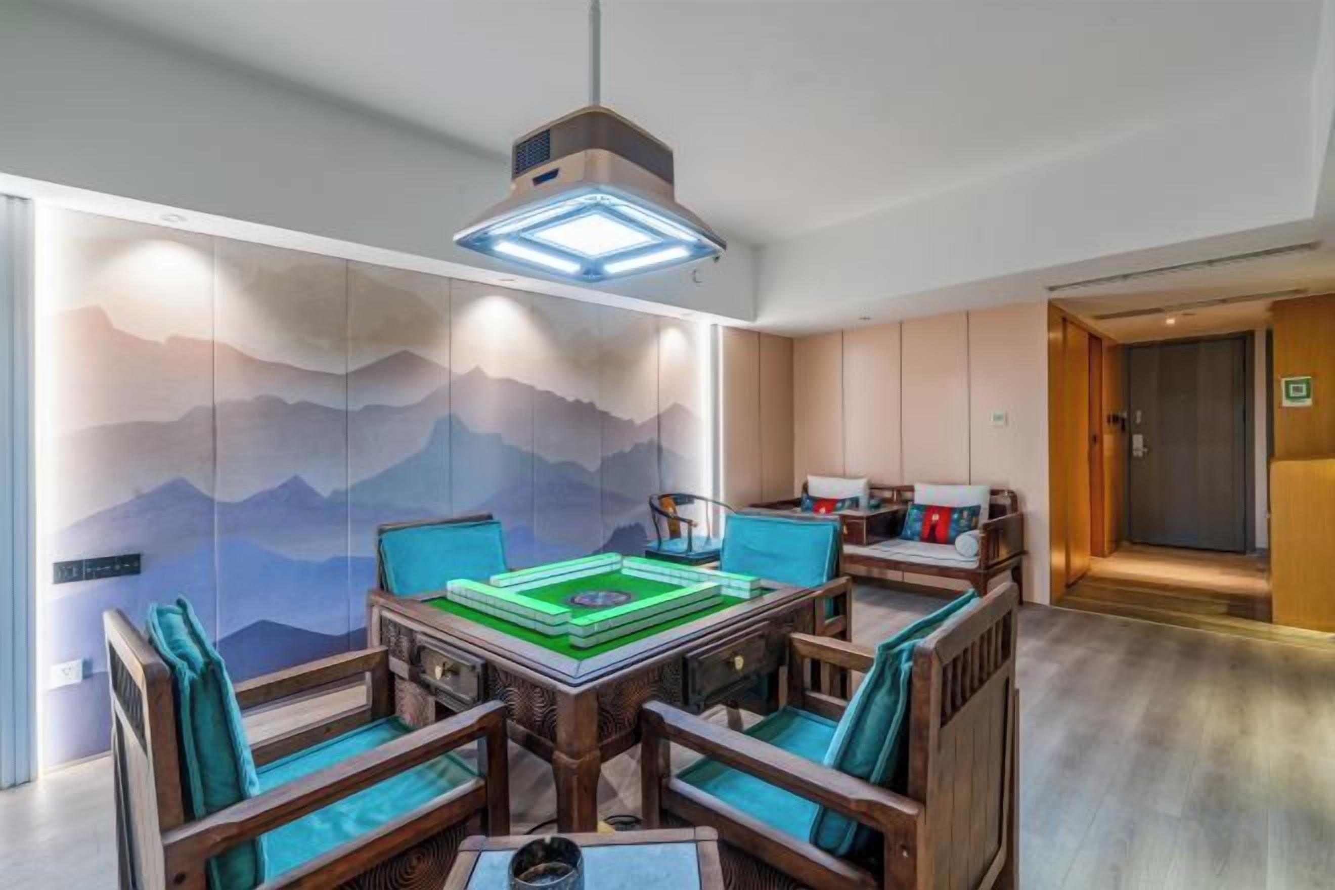 A room with a dining table, chairs, a hanging light fixture, and a wall with a mountain design.