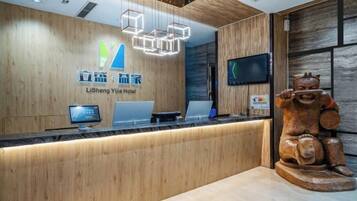 A hotel reception desk with a wooden finish, a digital screen, and a traditional wooden statue.
