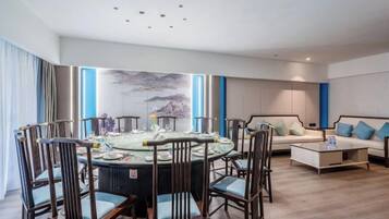 Quarto de hotel moderno com mesa de jantar redonda, cadeiras, sofá e mesa de centro.